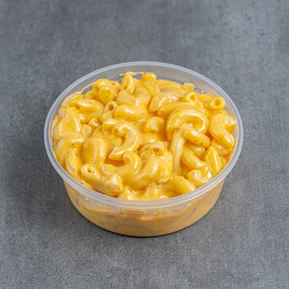 Clear container filled with creamy macaroni and cheese on a dark gray surface.