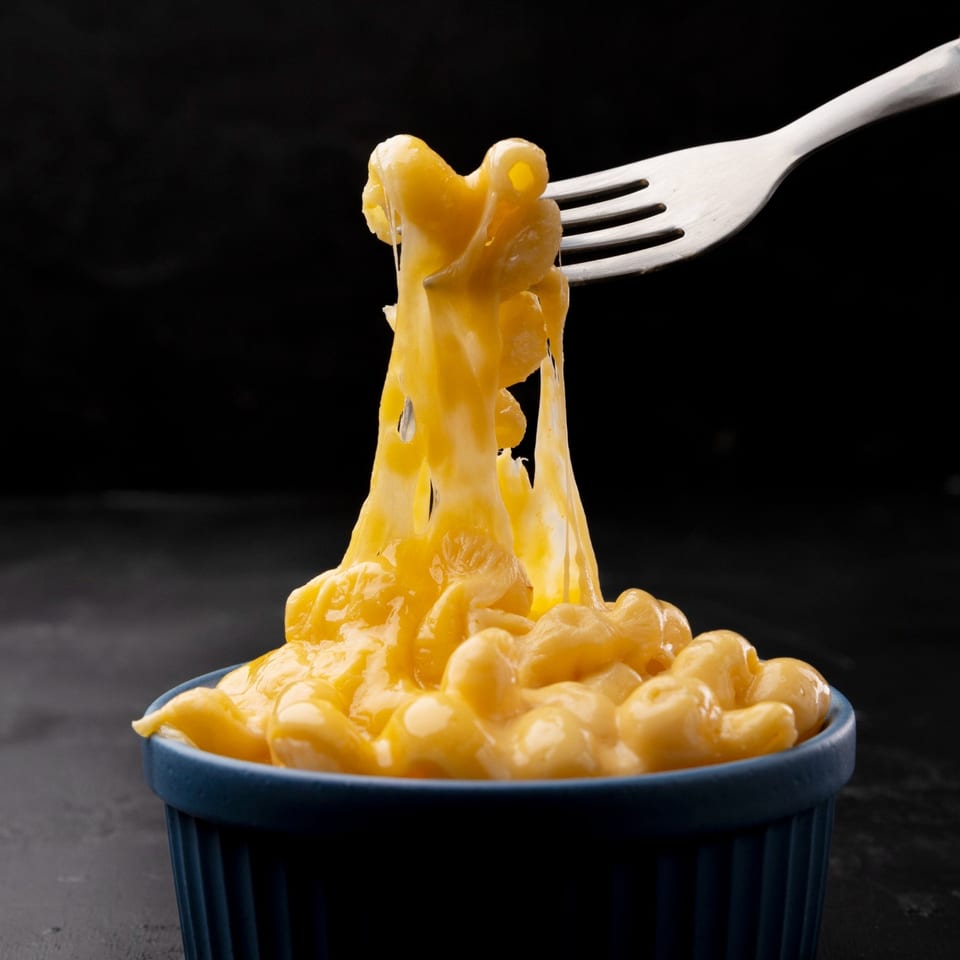 Fork lifting gooey, cheese-covered macaroni from a dark blue bowl against a black background.