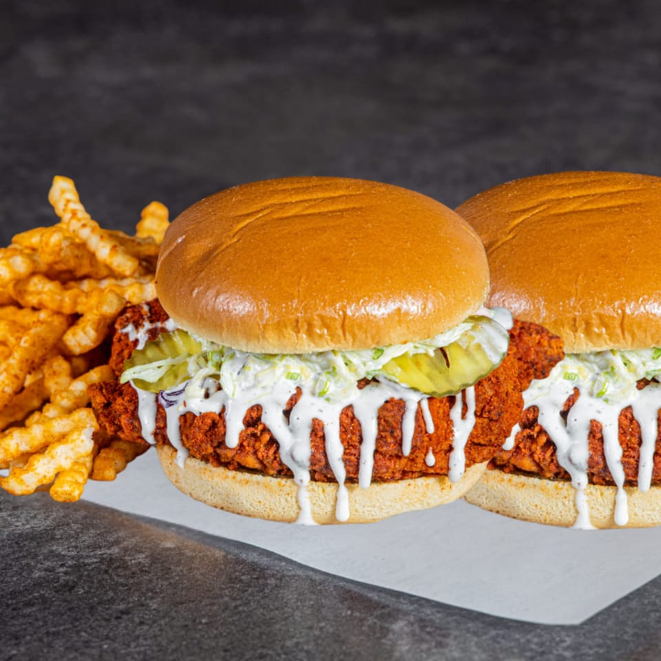 Two crispy fried chicken sandwiches with pickles, shredded lettuce, and creamy sauce served with seasoned waffle fries.