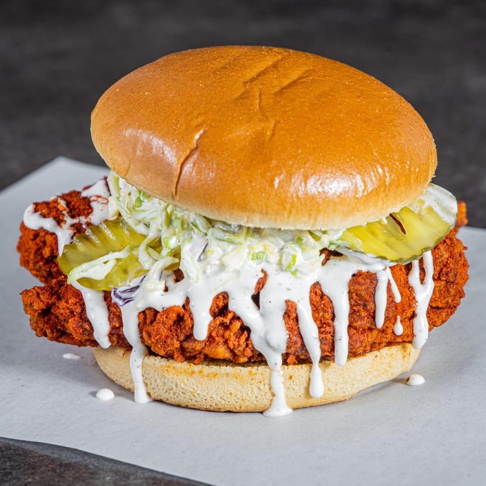 Crispy fried chicken sandwich with pickles, creamy slaw, and white sauce on a toasted bun.