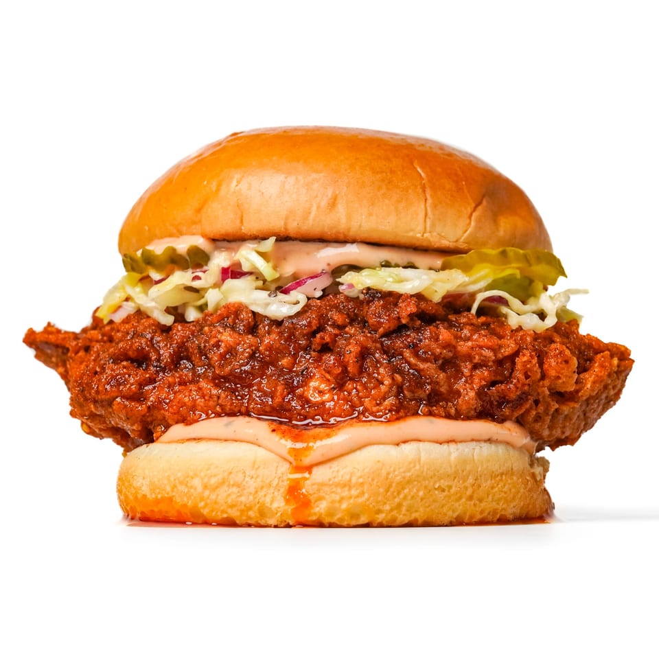 Close-up of a crispy fried chicken sandwich with shredded lettuce, pickles, creamy sauce, and a glossy brioche bun.